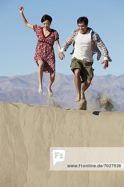 Couple jumping on sand  mountains in background