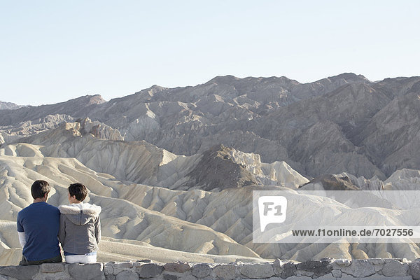 Couple sitting on stone wall in desert (rear view)  Death Valley  California  USA