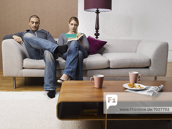 Young woman reading book and young man listening to MP3 player on sofa