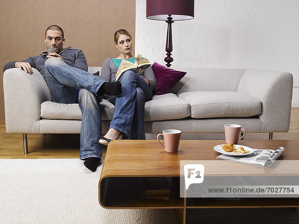 Young woman reading book and young man listening to MP3 player on sofa
