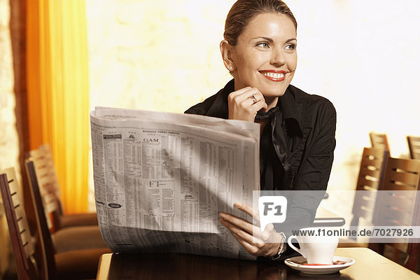 Mid adult woman reading newspaper in cafe
