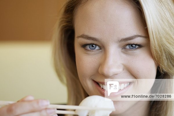 Junge Frau isst mit Stäbchen