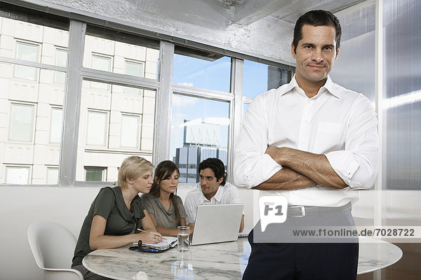 Male manager with colleagues using laptop in background (portrait)