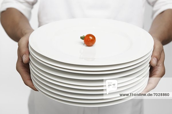 Chef holding stack of dinner plates with single cherry tomato on top (mid section)