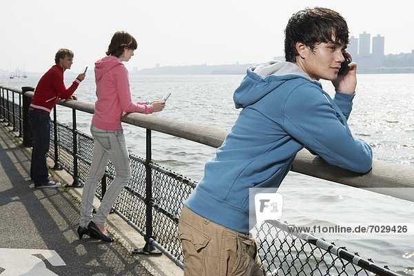Three teenagers using mobile phone at waterfront