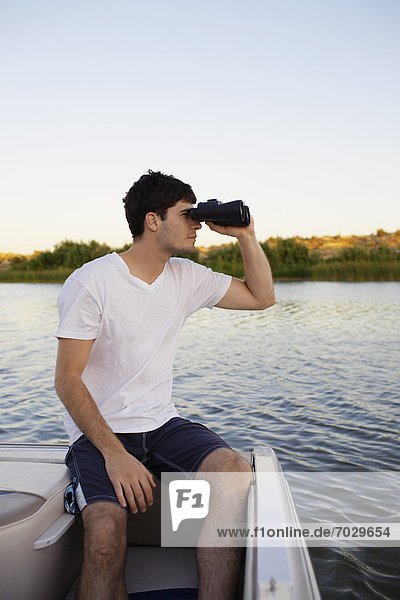Young man using binoculars at lake
