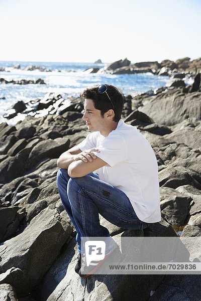 Young man sitting on rock by sea
