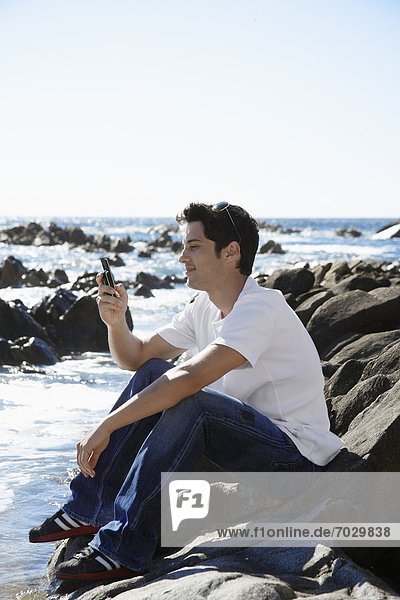 Young man using mobile phone by sea
