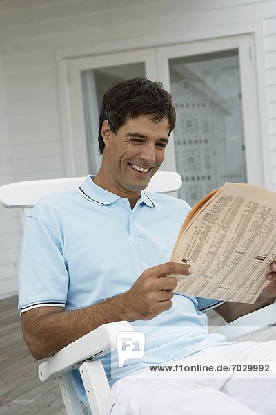 Mid adult man reading newspaper on lounge chair