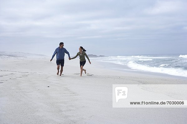 Mid adult couple running hand in hand on beach  Cape Town  South Africa