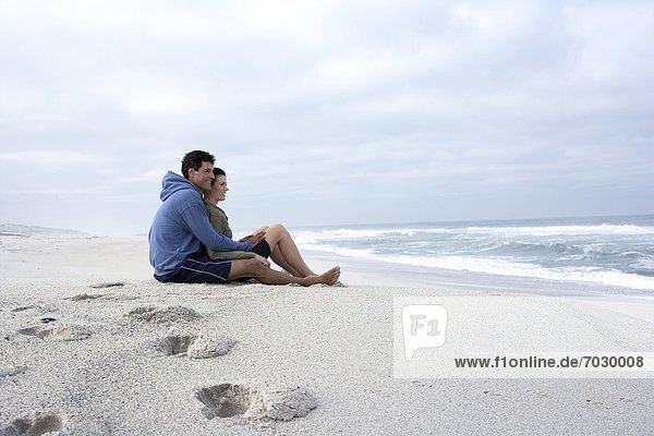 Mid adult couple sitting on sandy beach and looking at view  Cape Town  South Africa