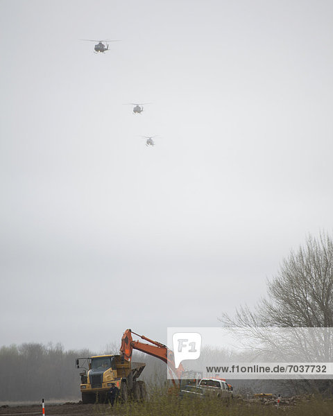 'Tractors And Trucks Working On The Riverbank To Prevent Flooding With Army Helicopters Approaching In The Air