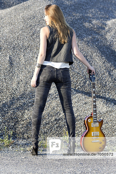 Junge Frau in Lederweste und Jeans posiert mit E-Gitarre
