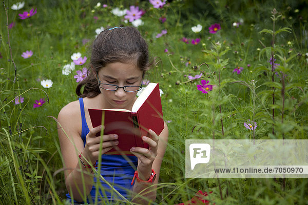 Mädchen  11 Jahre  liest ein Buch inmitten einer Blumenwiese in freier Natur