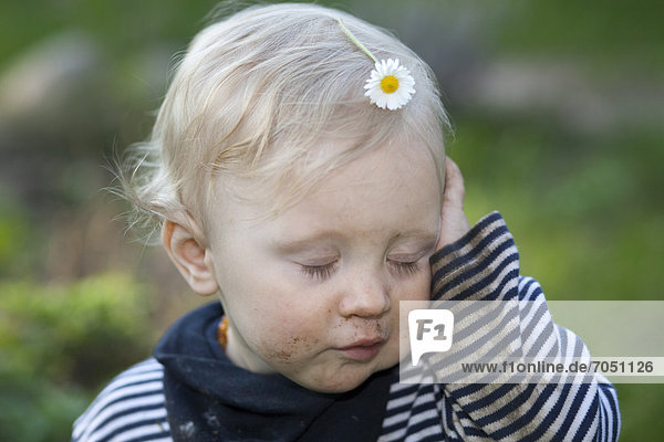 Kleiner müder Junge mit Gänseblümchen