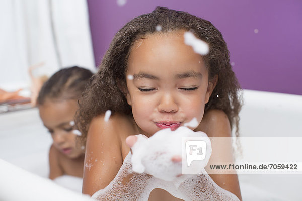 Mixed race girls playing with bubbles in bathtub