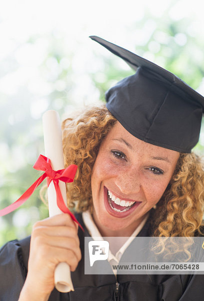Portrait of smiling young woman in mortarboard showing diploma