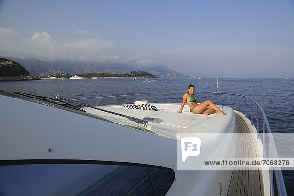 Young woman wearing a green bikini sitting on the front sun deck of a motor yacht  French Riviera  Cote d'Azur  Mediterranean Sea  Europe