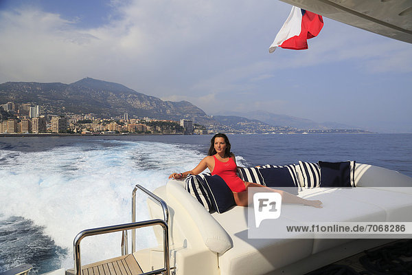 Young woman wearing a red swimsuit sitting on the back deck of a motor yacht  in front of Monaco  French Riviera  Cote d'Azur  Mediterranean Sea  Europe