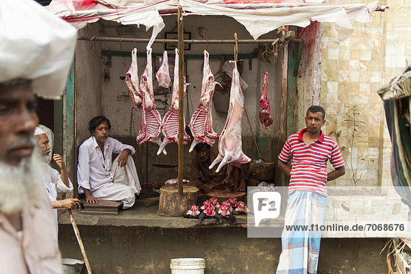Straßen-Schlachterei  abgezogene Tiere hängen von Balken  rohes Fleisch liegt darunter  Schlachter wartet auf Kundschaft  Dhaka  Bangladesch  Südasien
