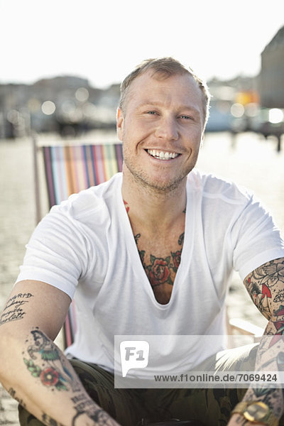 Portrait of a happy tattooed man sitting in deck chair at beach