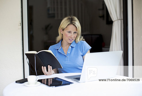 Mid adult woman with laptop and digital tablet holding book