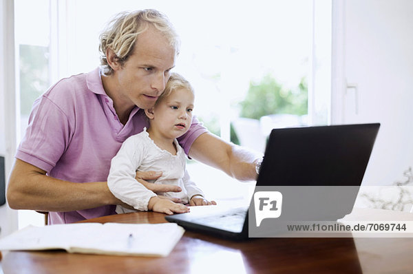 Mittlerer erwachsener Mann mit Laptop und Tochter am Schreibtisch