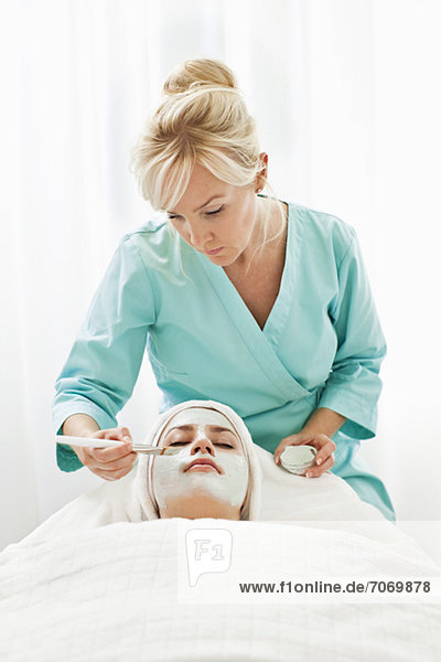 Blonde Kosmetikerin mit Gesichtsmaske für junge Kunden im Beauty Spa