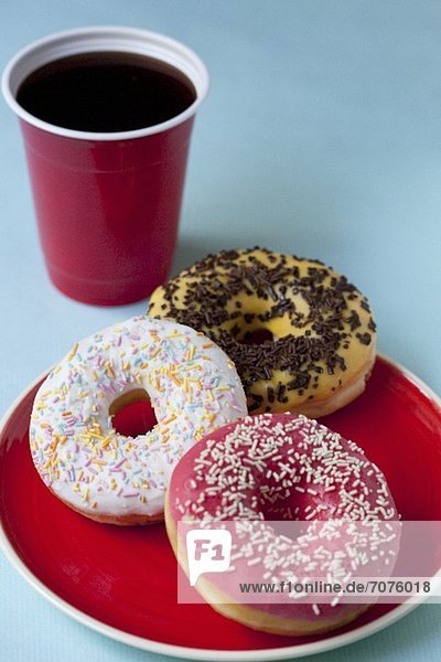 Glasierte Doughnuts mit Zucker- und Schokostreuseln und ein Becher Kaffee