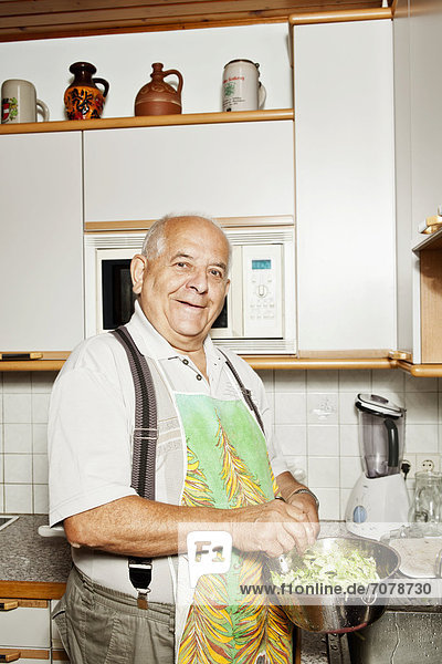 Elderly man preparing a salad in the kitchen