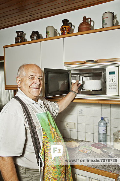 Älterer Mann kocht mit Mikrowellenherd