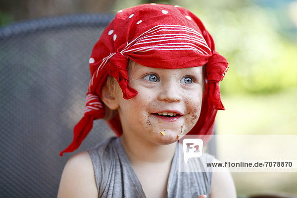 Young boy wearing a scarf on his head with his mouth smeared with chocolate