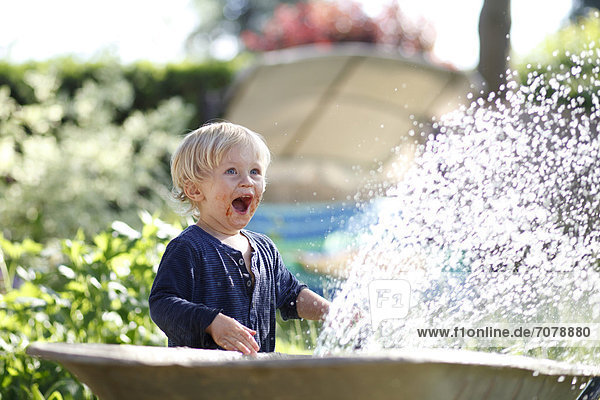 Young boy with his mouth smeared with chocolate playing with a garden hose and laughing