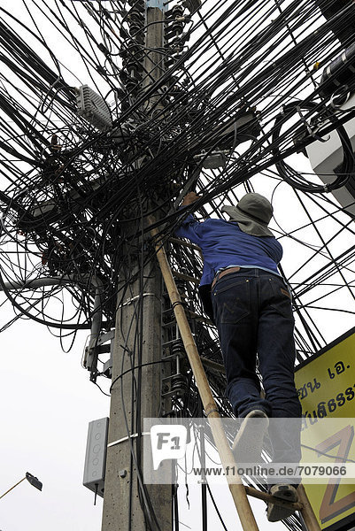Mann klettert eine Leiter hoch an einem Stromleitungsmasten  Chiang Mai  Thailand  Asien