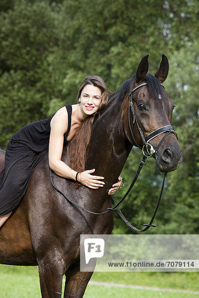 Junge Frau mit Kleid sitzt auf Pferd  schmust mit Pferd  Hannoveraner  Brauner  Nordtirol  Österreich  Europa