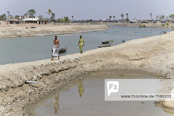Man and a woman walking along a dam  Cyclone Aila severely flooded the town of Gabura in 2009  Sundabarns  Khulna District  Bangladesh  South Asia  Asia