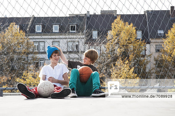 Zwei Jungen sitzen auf einem Sportplatz mit Bällen