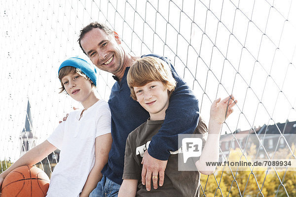 Vater und zwei Söhne mit Basketball auf einem Sportplatz
