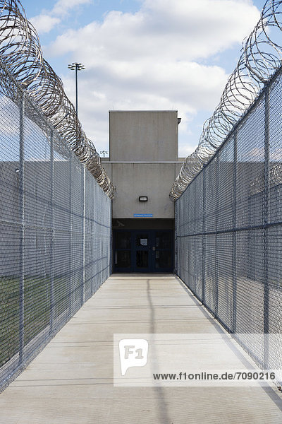 Prison fence and barbed wire at exit of a Correctional Facility. A narrow walkway with high fencing  and coiled razor wire.