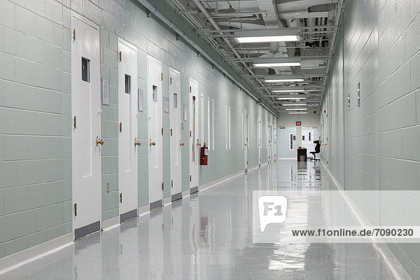 Hallway and prison cells along a corridor. Observation hatches in the doors. A Correctional Facility. A desk and table at the end.