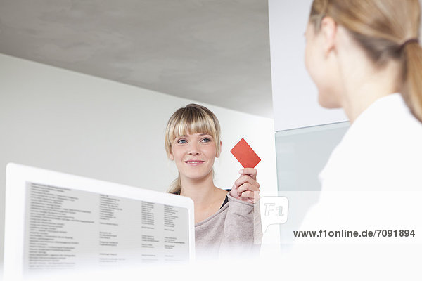 Germany  Patient giving insurance card to receptionist in dental office