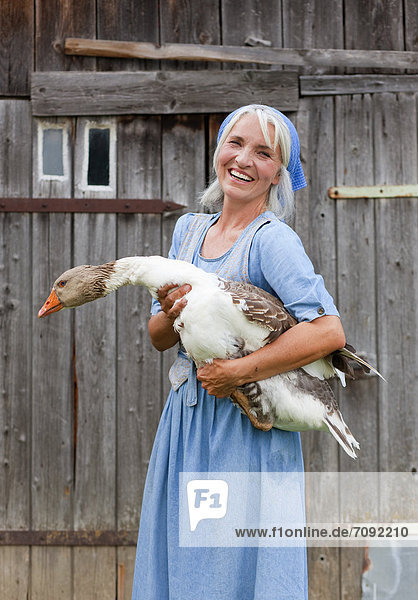 Mature woman with goose on farm