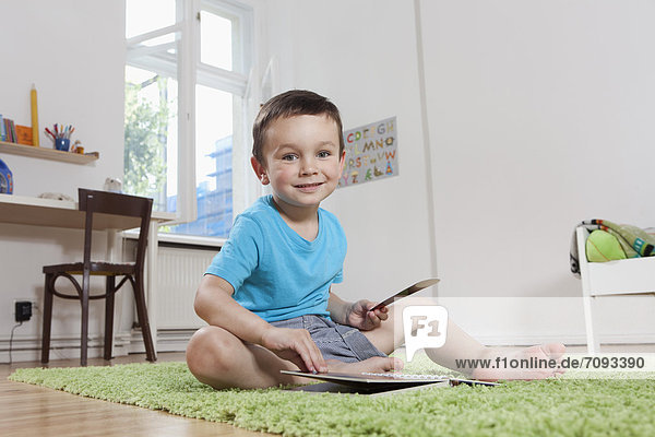 Boy sitting on floor with book  smiling  portrait