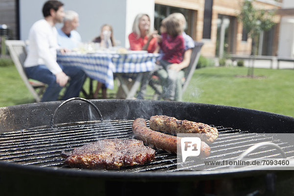 Germany  Bavaria  Nuremberg  Close up of barbecue  family sitting in background