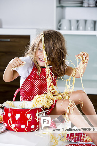 Germany,  Girl playing with spaghetti on kitchen worktop