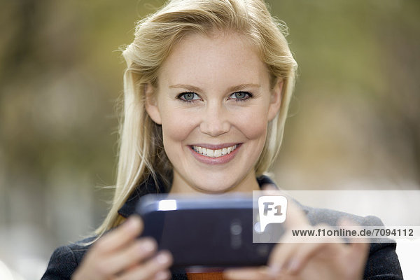 Europa  Deutschland  Nordrhein-Westfalen  Düsseldorf  Junge Frau mit Smartphone  lächelnd  Portrait