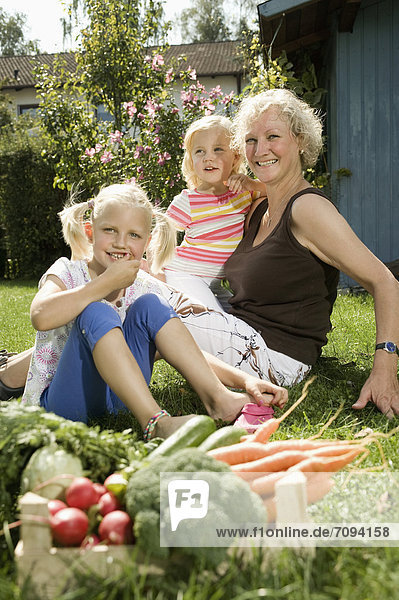 Germany  Bavaria  Grandmother with children sitting in garden  vegetables in foreground
