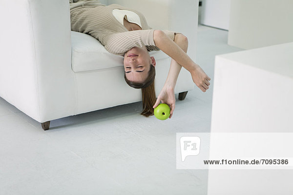 Woman lying upside down on sofa  holding apple