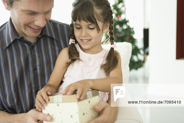 Kleines Mädchen eröffnet Weihnachtsgeschenk mit Vater