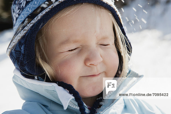 Kleinkind Mädchen in Winterkleidung im Schnee mit geschlossenen Augen  Portrait